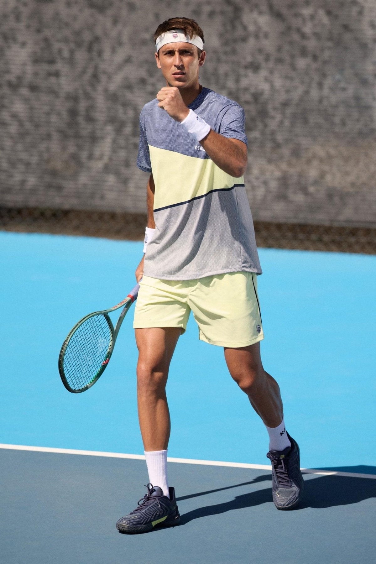 Man on a tennis court wearing a colorful shirt and yellow shorts, holding a tennis racket.