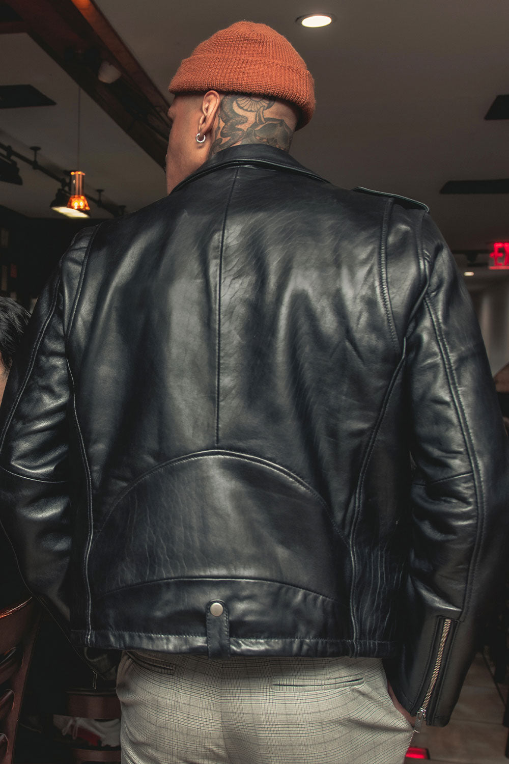 Person wearing a black leather jacket and orange beanie in an indoor setting