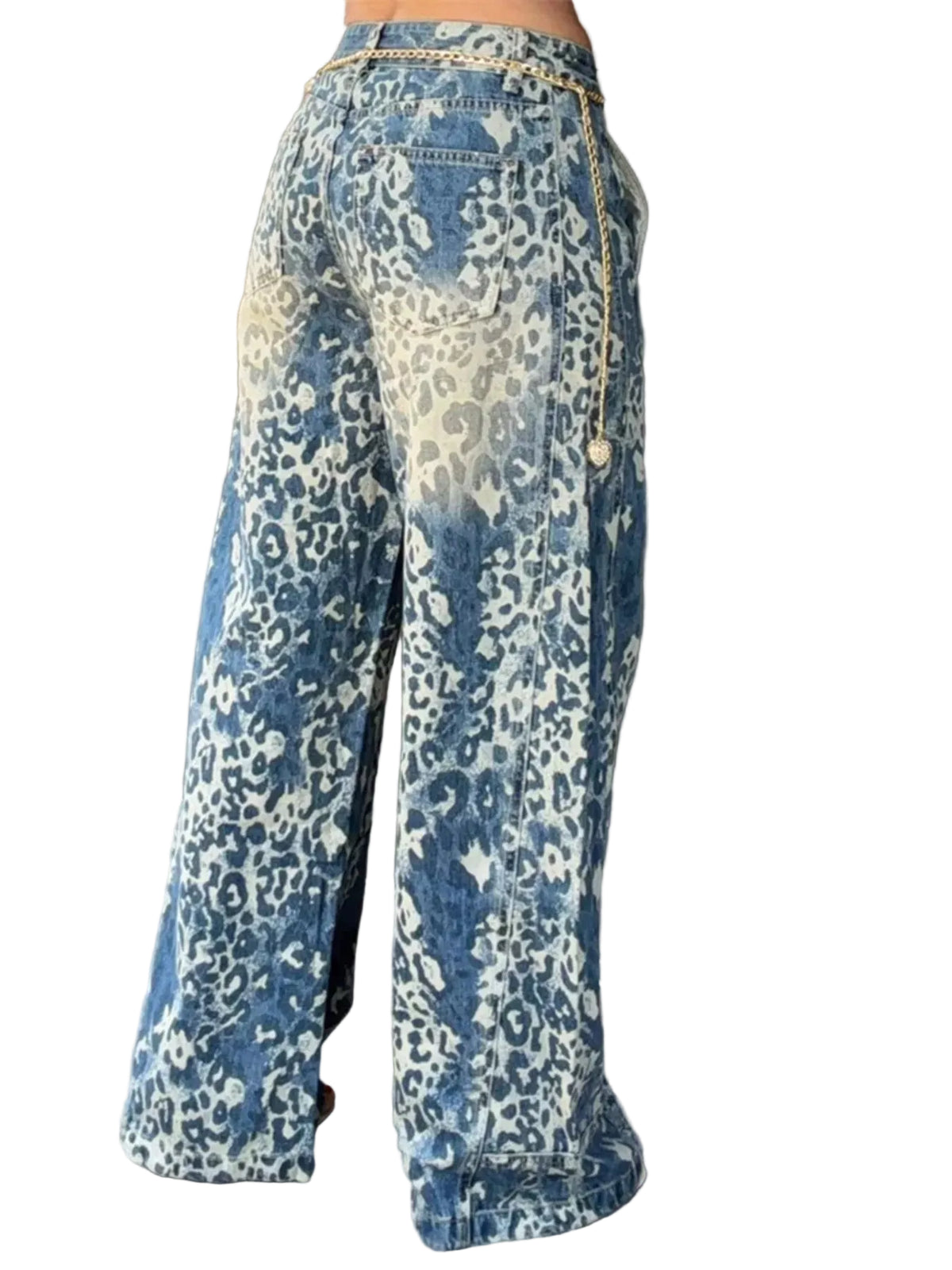 Wide-leg denim pants with a blue and off-white leopard print pattern, featuring a gold chain detail along the side, shown on a model standing against a dark brown paneled wall.