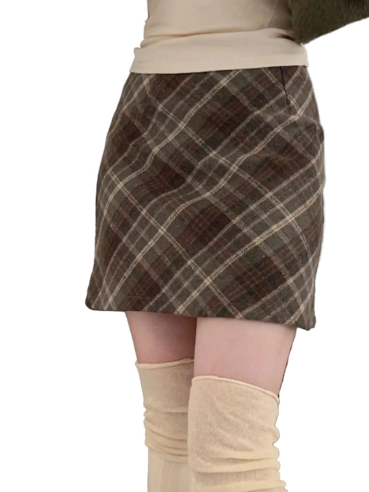 A person wearing a brown and beige plaid mini skirt with cream knee-high socks, standing in front of a gray textured sofa.