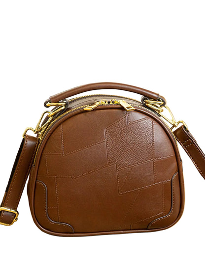 A brown leather dome-shaped handbag with geometric stitched paneling and gold-tone hardware, displayed on a light wood surface with a Chanel perfume bottle in the background.
