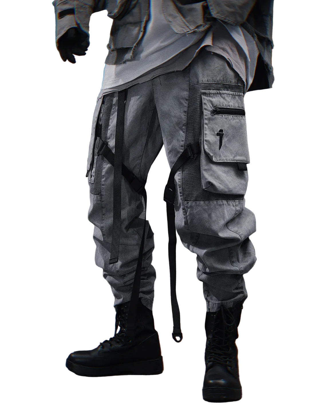 A person wearing loose, oversized cargo-style pants in a washed gray tone, styled with black combat boots and dark gloves, standing against a textured gray wall.