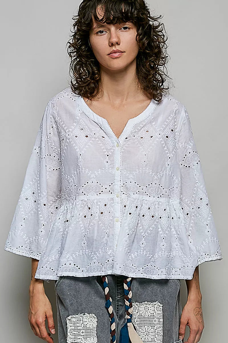Woman wearing a white embroidered blouse against a gray background