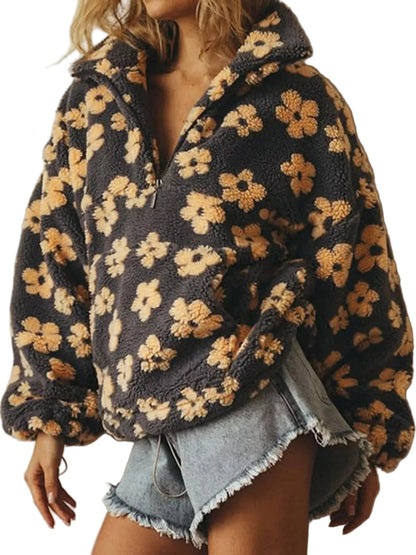 A woman wearing a dark charcoal gray fuzzy fleece pullover jacket with a tan and beige floral pattern, paired with frayed denim shorts.