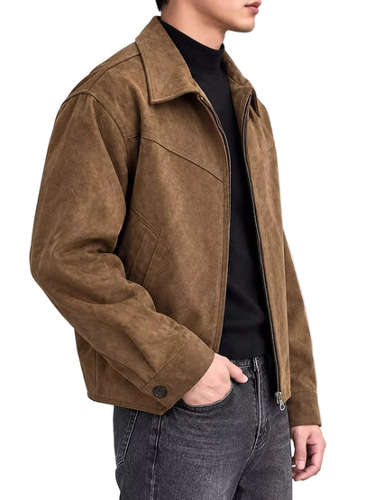 A man wearing a brown suede jacket over a black turtleneck sweater and dark gray jeans, shown from the side against a light gray studio background.