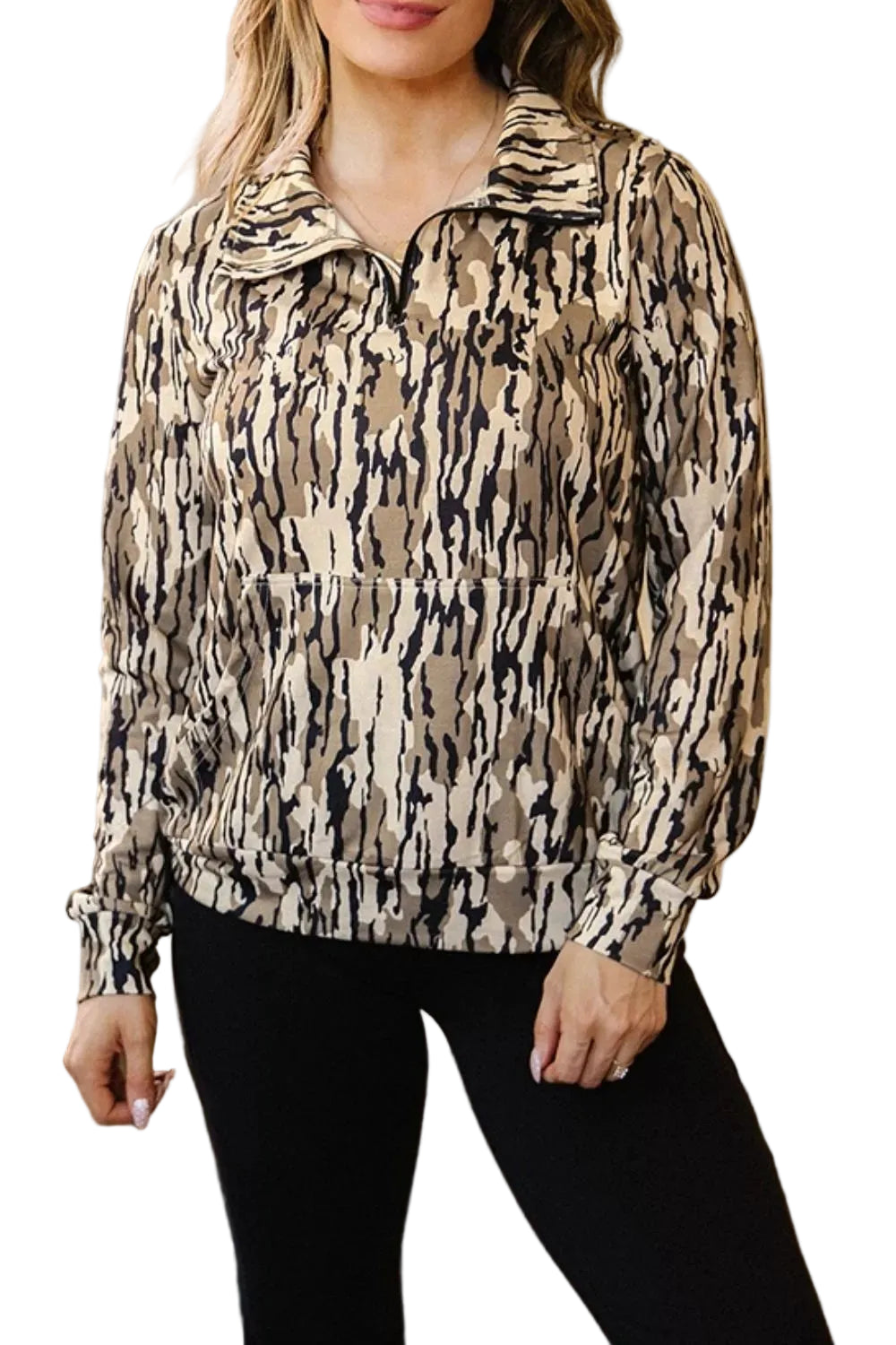 A woman wearing a beige, black, and brown abstract patterned half-zip pullover jacket with black leggings, standing in an indoor setting.