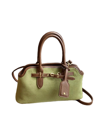 A structured light green canvas handbag with brown leather handles, trim, and hardware, resting on a wooden surface next to white window blinds.