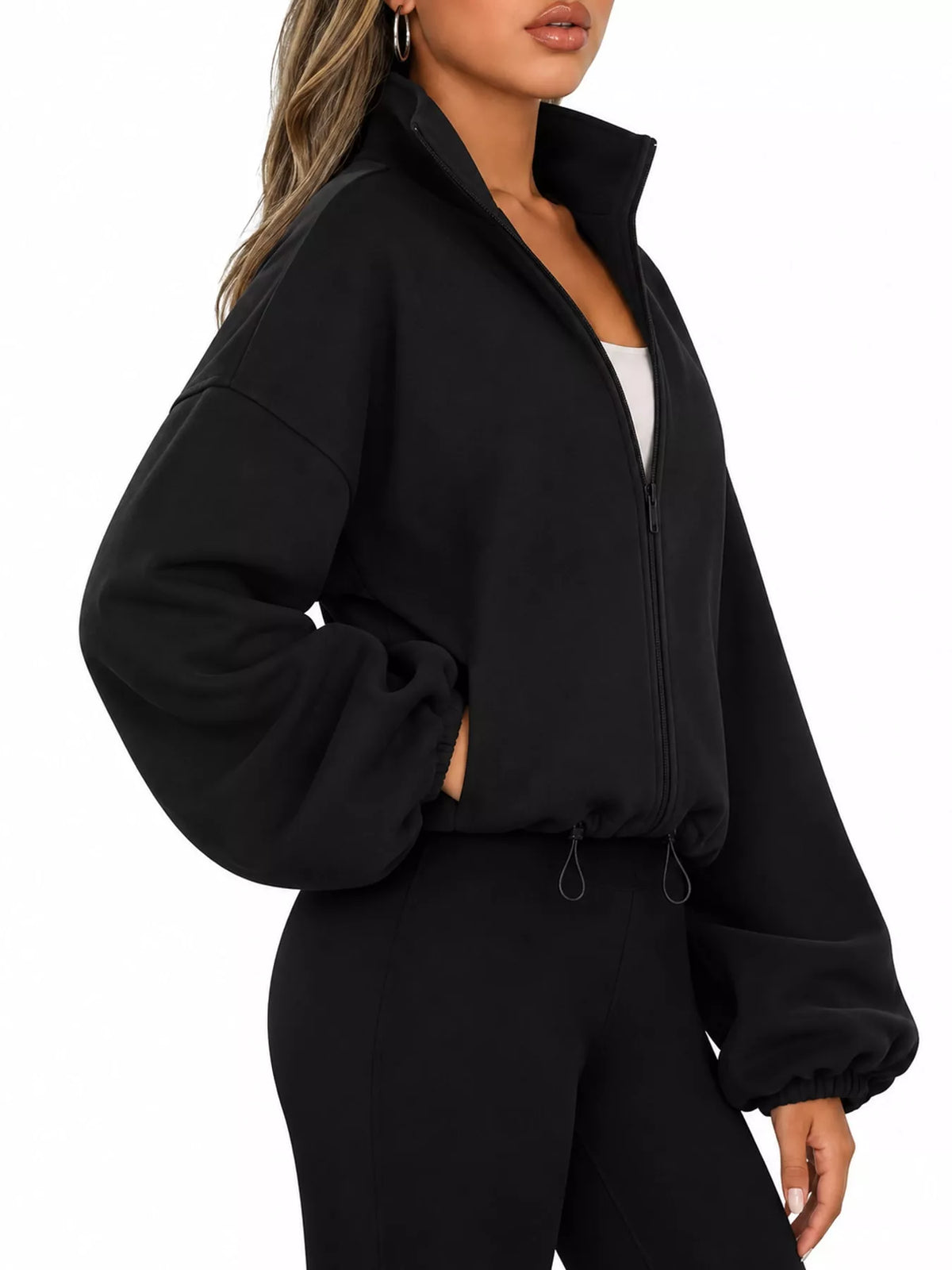 A woman wearing a black cropped zip-up jacket with balloon sleeves and matching black pants, shown against a plain white background.