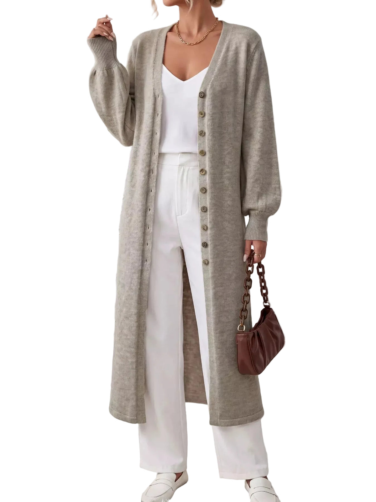 A woman models a long, light gray cardigan with brown buttons over a white top and white wide-leg pants, holding a brown handbag against a textured white wall.