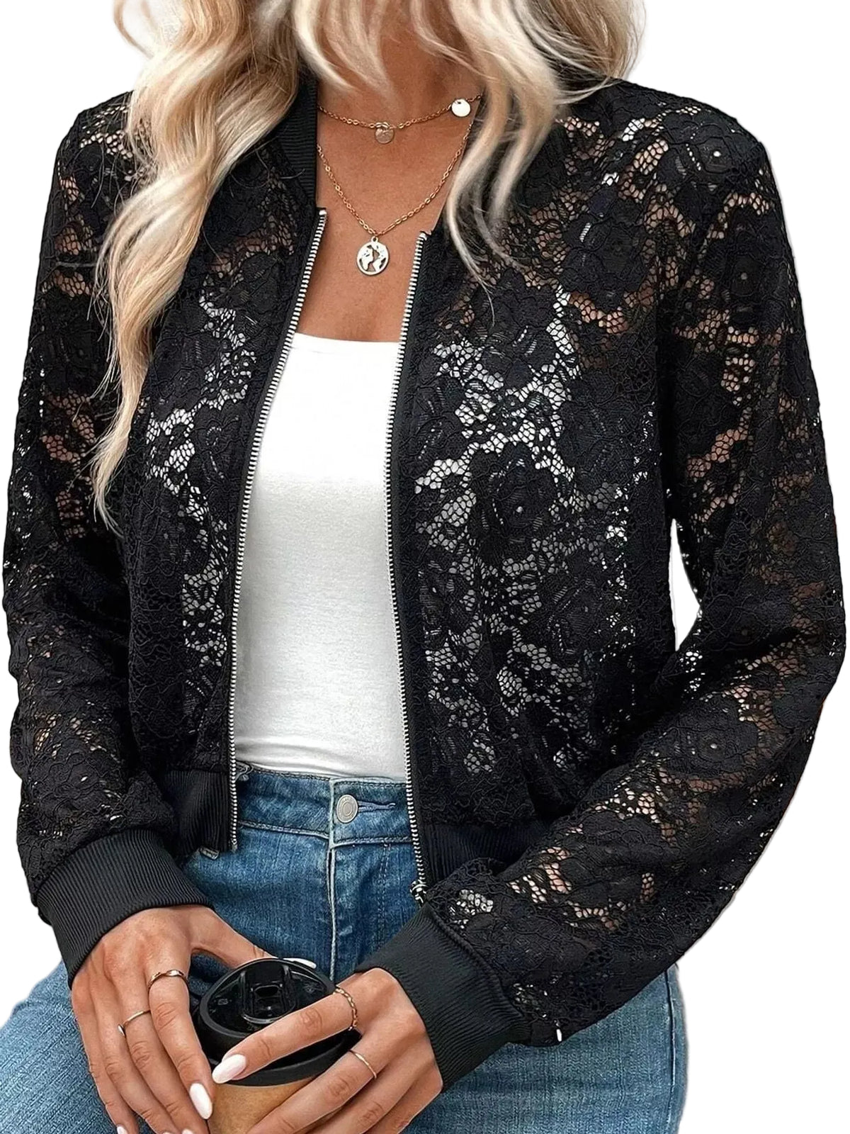 A woman wearing a black lace bomber jacket over a white tank top and blue jeans, holding a coffee cup.