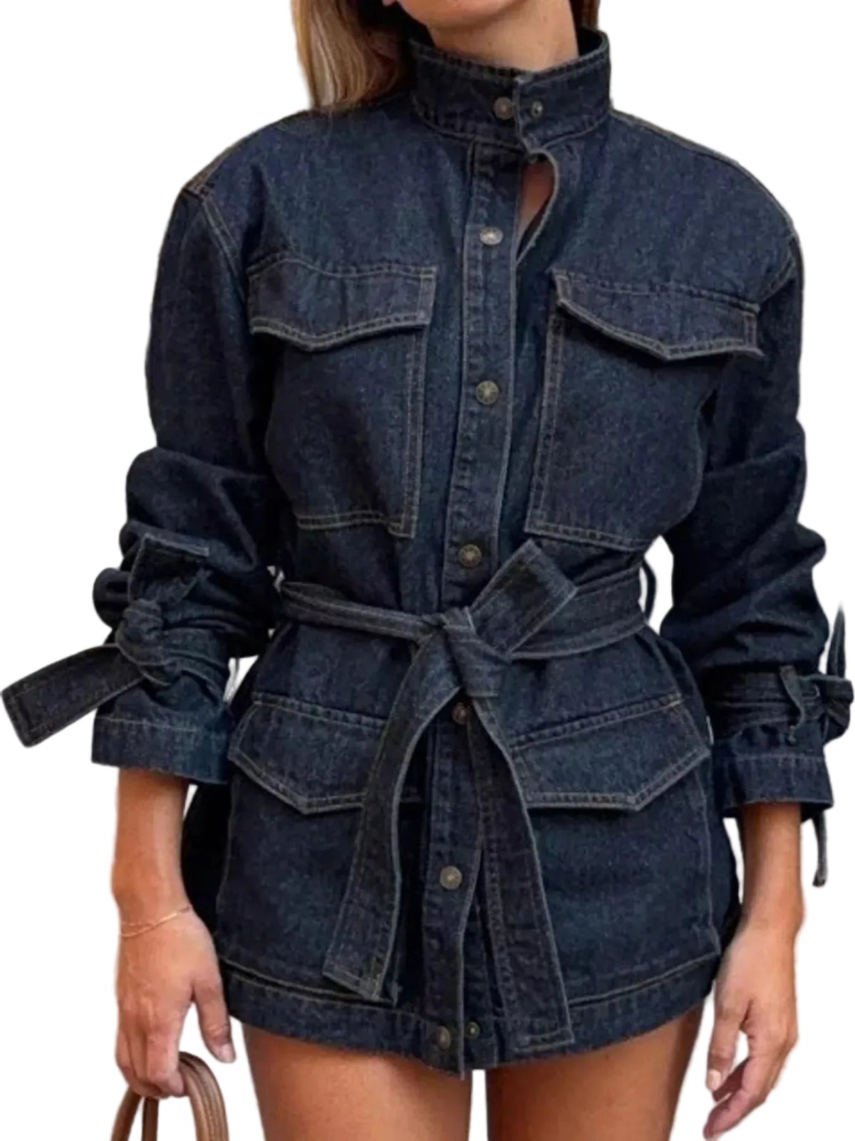 A woman wearing a dark blue denim mini jacket with a high collar, button front, chest flap pockets, and a matching tie belt, photographed outdoors on a cobblestone street.