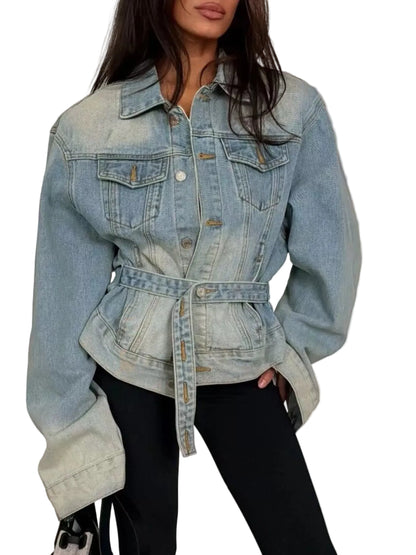 A woman wearing a light-wash blue denim jacket with a belted waist and front flap pockets, paired with black pants.