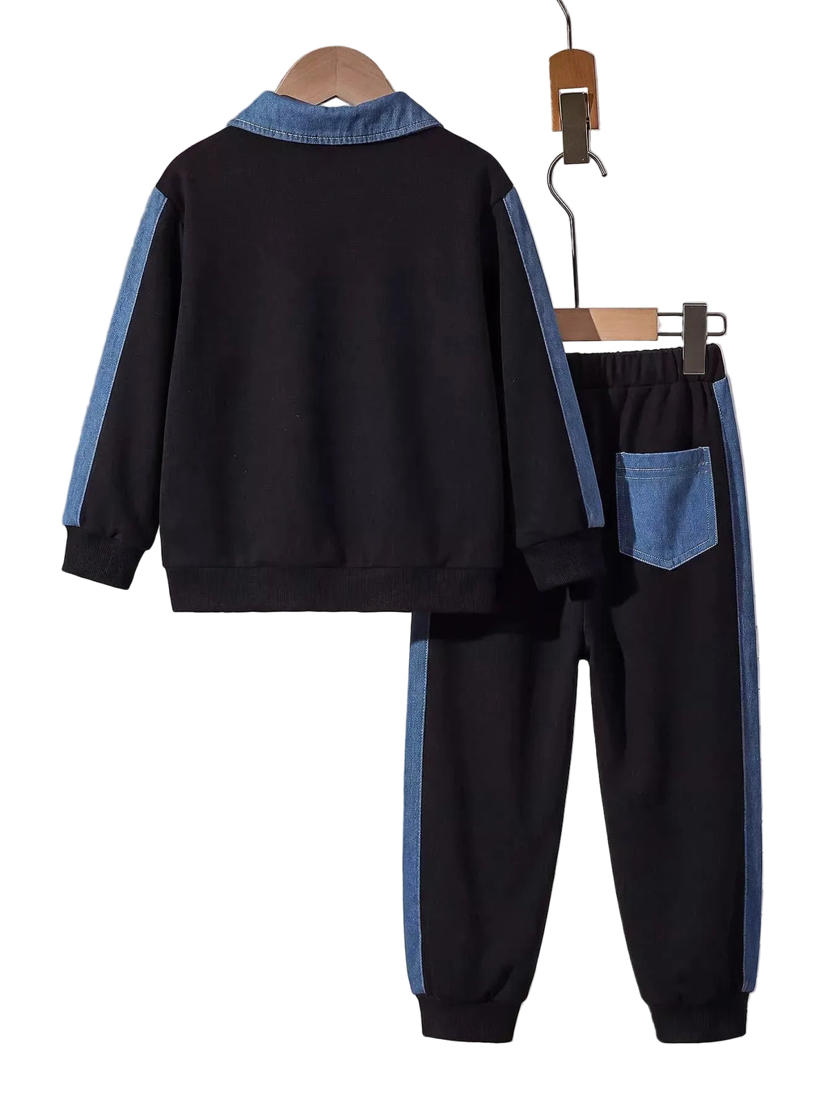 A two-piece kids' tracksuit set consisting of a black long-sleeve top with light blue contrast panels on the collar and sleeves, and matching black pants with light blue side stripes and a blue back pocket, displayed on wooden hangers against a gray wall with books in the background.