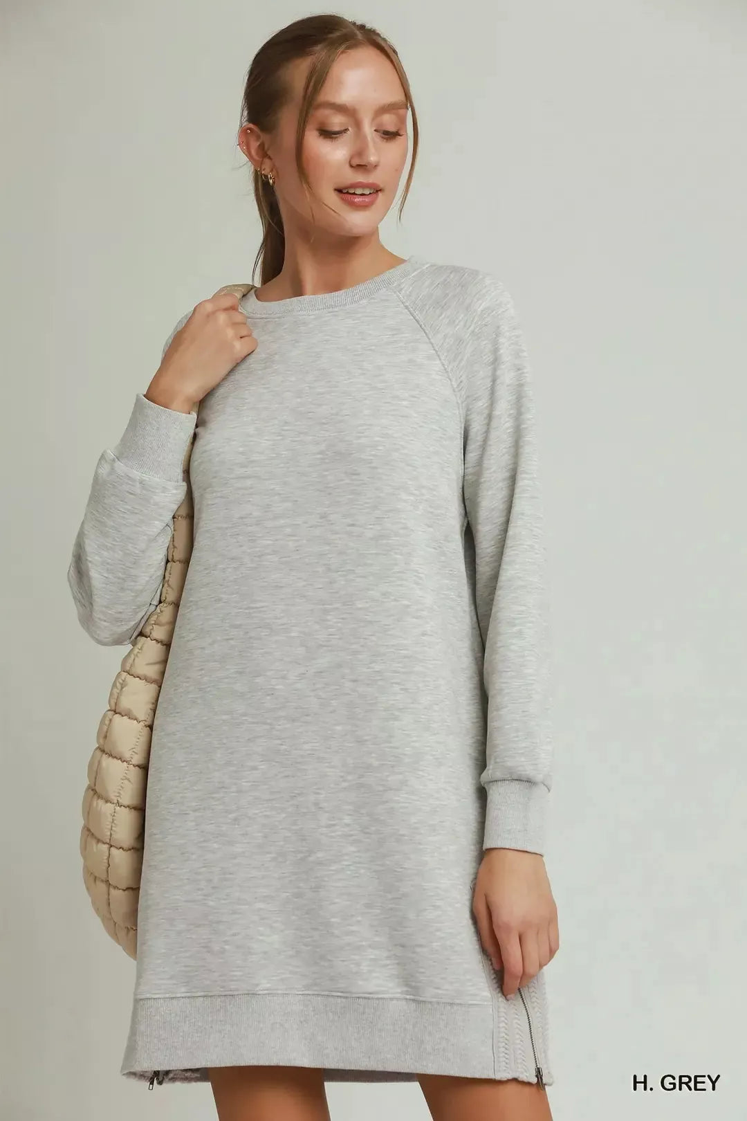 Woman wearing a gray dress with a beige quilted bag on a plain background