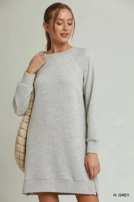Woman wearing a gray dress with a beige quilted bag on a plain background