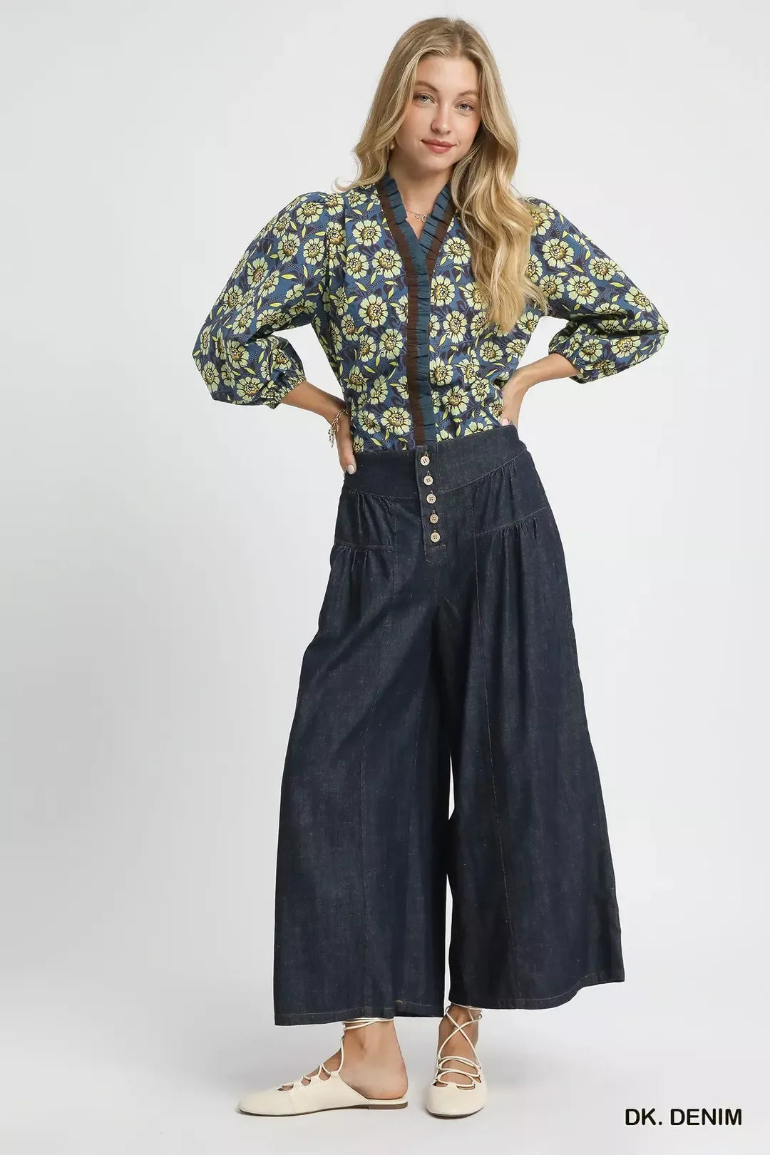 Woman wearing a floral blouse and denim wide-leg pants on a white background