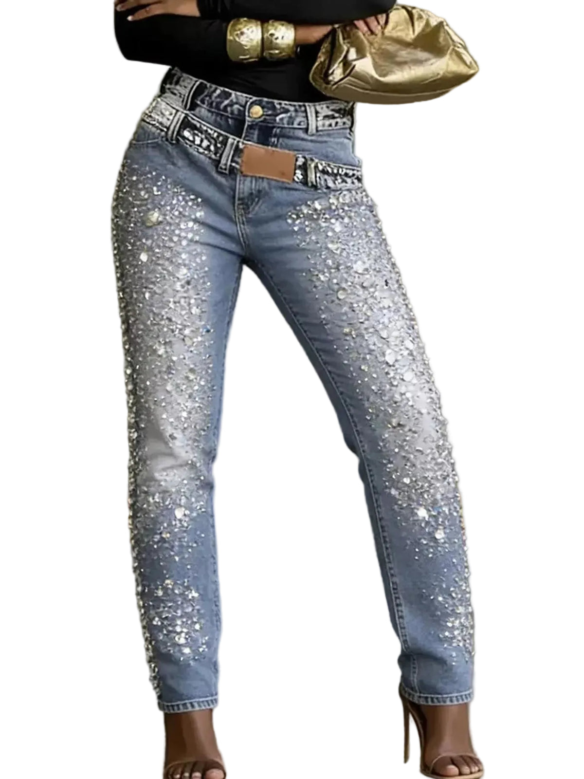 Light-wash blue jeans covered in sparkling silver rhinestone embellishments, worn with a black top and brown high-heeled sandals, with a gold clutch bag held at the hip.