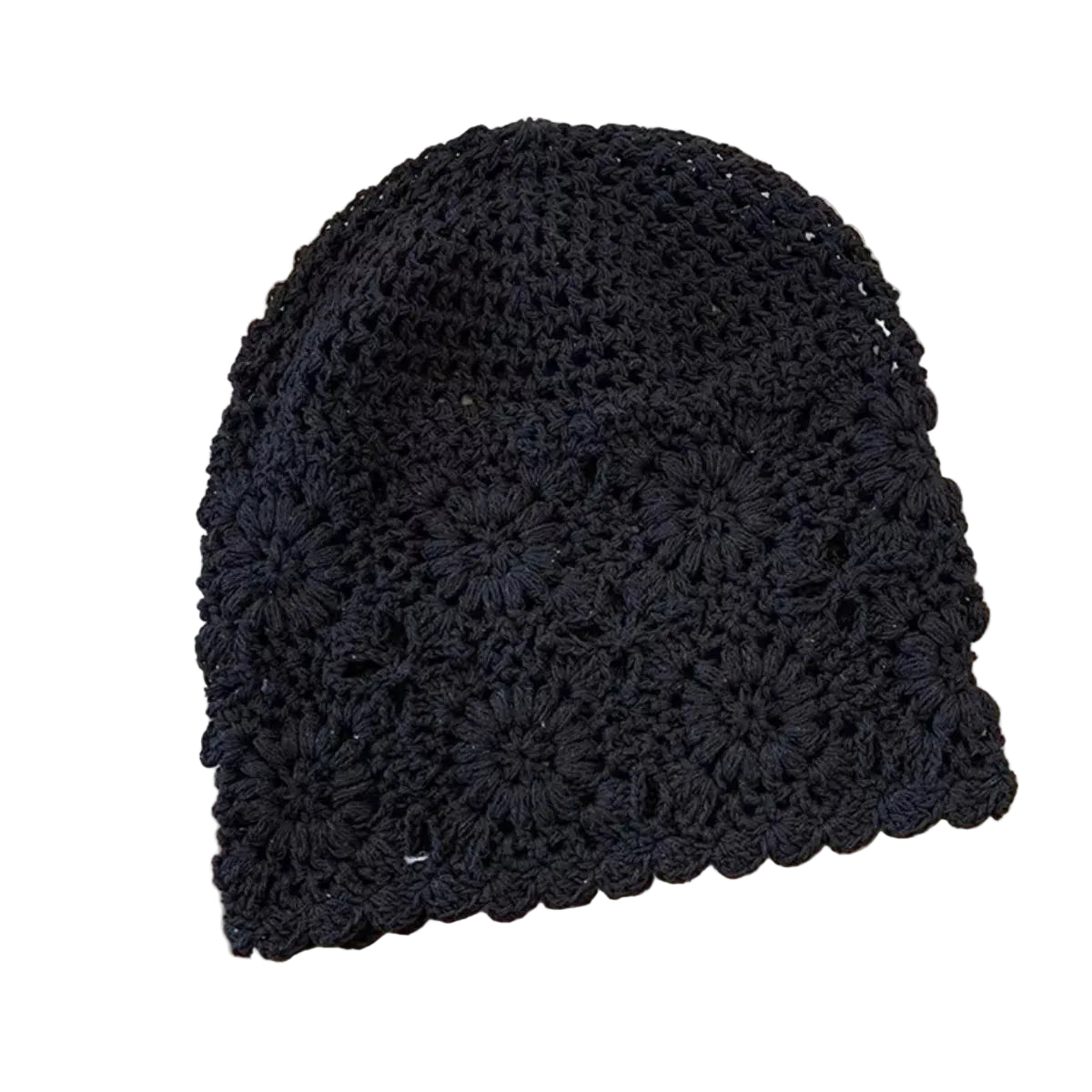 A black crocheted beanie hat with a textured floral pattern and scalloped edge, laid flat on a light wood surface with a cream fabric and striped cloth in the background.