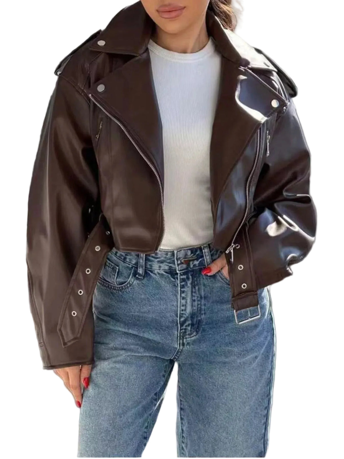 A woman wearing a shiny dark brown faux-leather moto jacket over a white ribbed top and blue jeans, standing against a gray slatted wall.