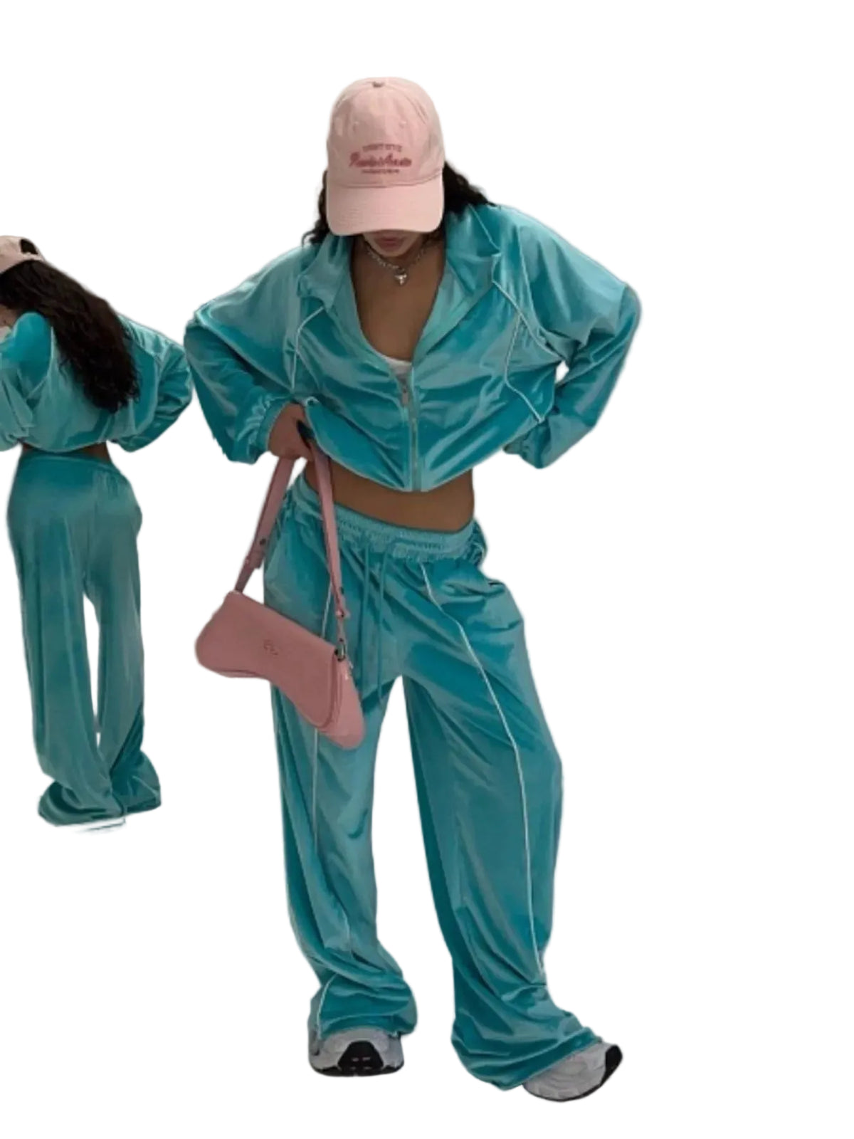 A person modeling a matching turquoise-blue velour tracksuit with white piping, a pink baseball cap, and a pink shoulder bag in a studio setting.
