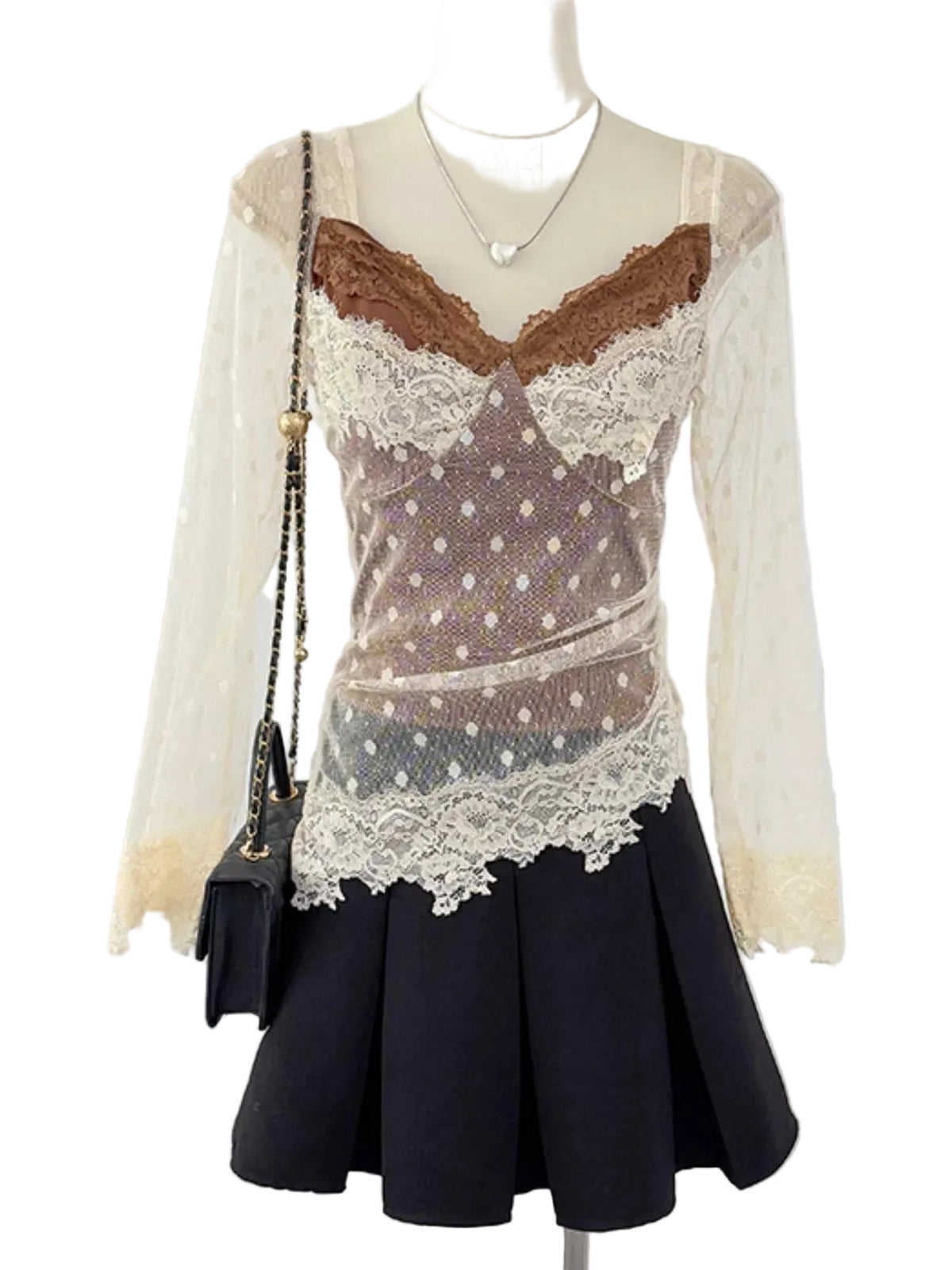 A long-sleeve lace top displayed on a mannequin, featuring a sheer brown polka-dot mesh body with cream lace trim and a brown lace neckline, paired with a black pleated skirt and a small black shoulder bag.