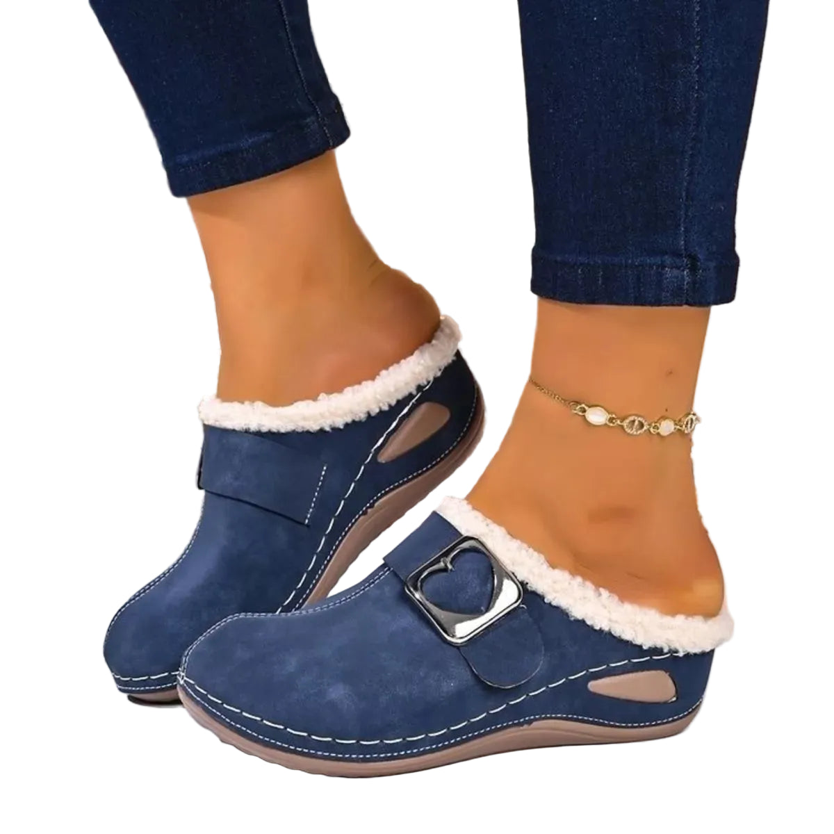 A pair of navy blue slip-on mule loafers with white sherpa lining and a silver heart-shaped buckle, shown on a model's feet with blue jeans.