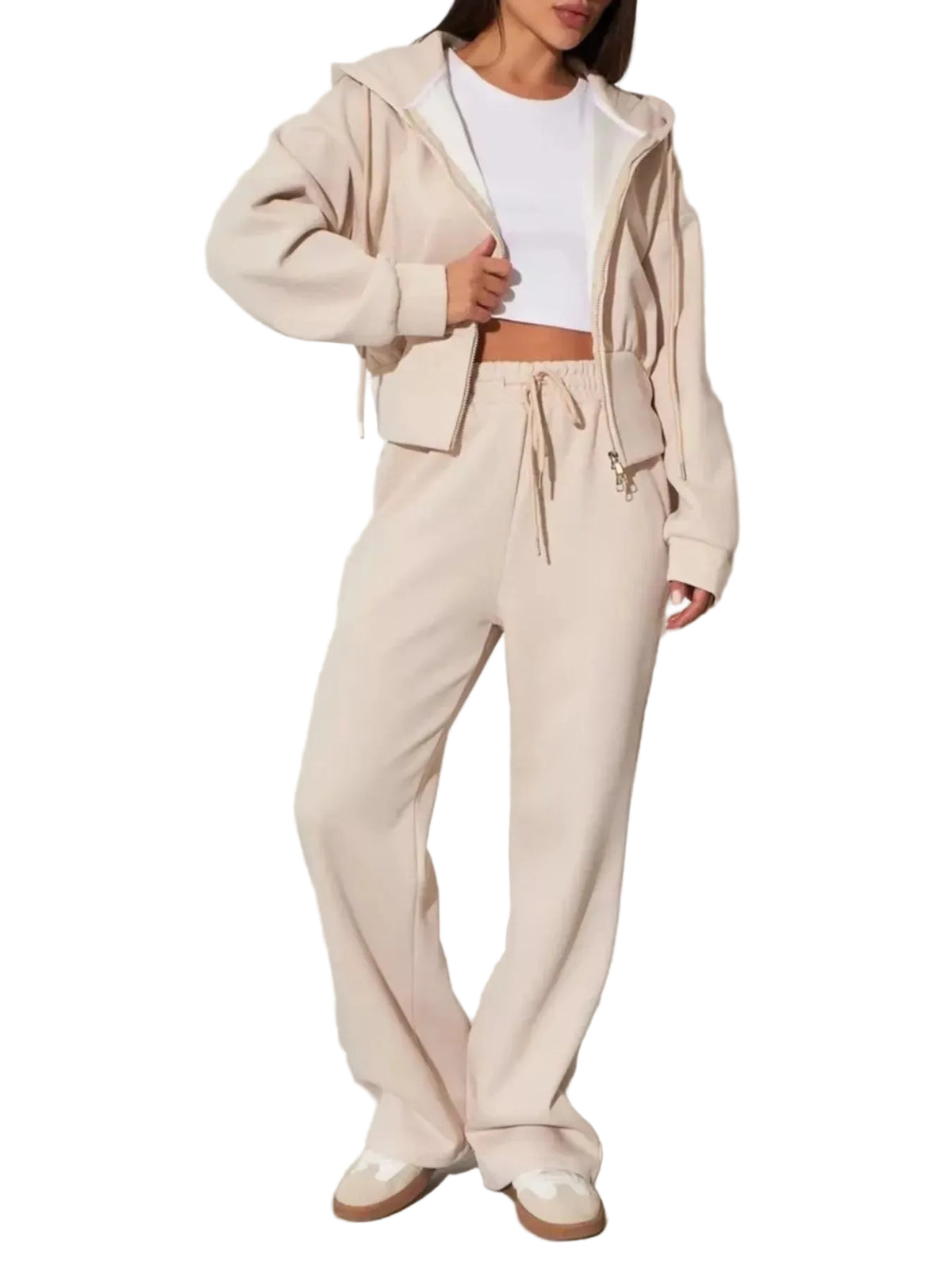 A model wearing a matching beige lounge set consisting of a cropped zip-up hoodie and wide-leg sweatpants, styled with a white crop top and white sneakers against a white wall.