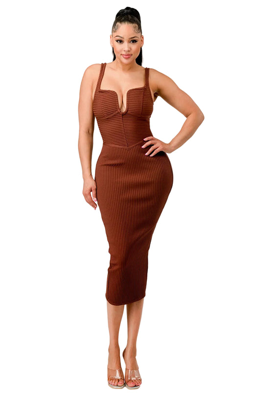 A woman modeling a ribbed brown midi dress with a plunging V-neckline and wide shoulder straps, paired with clear high-heeled sandals, against a plain light gray studio background.
