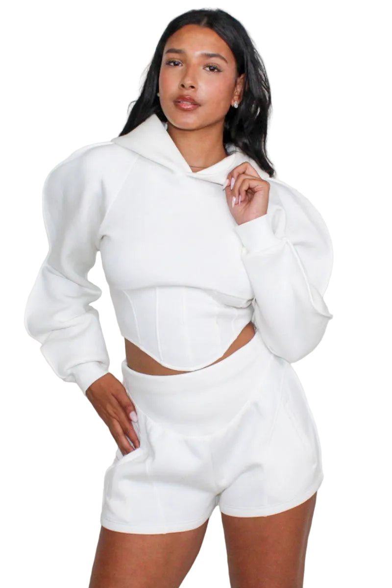 Woman wearing a white hoodie and shorts set against a plain background