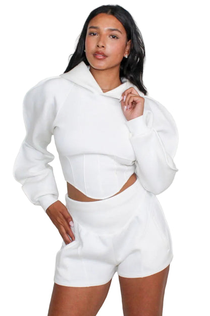 Woman wearing a white hoodie and shorts set against a plain background