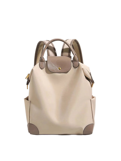 A beige leather backpack with taupe-brown accents, dual top handles, side pockets, and gold-tone hardware, photographed against a clean light gray background.