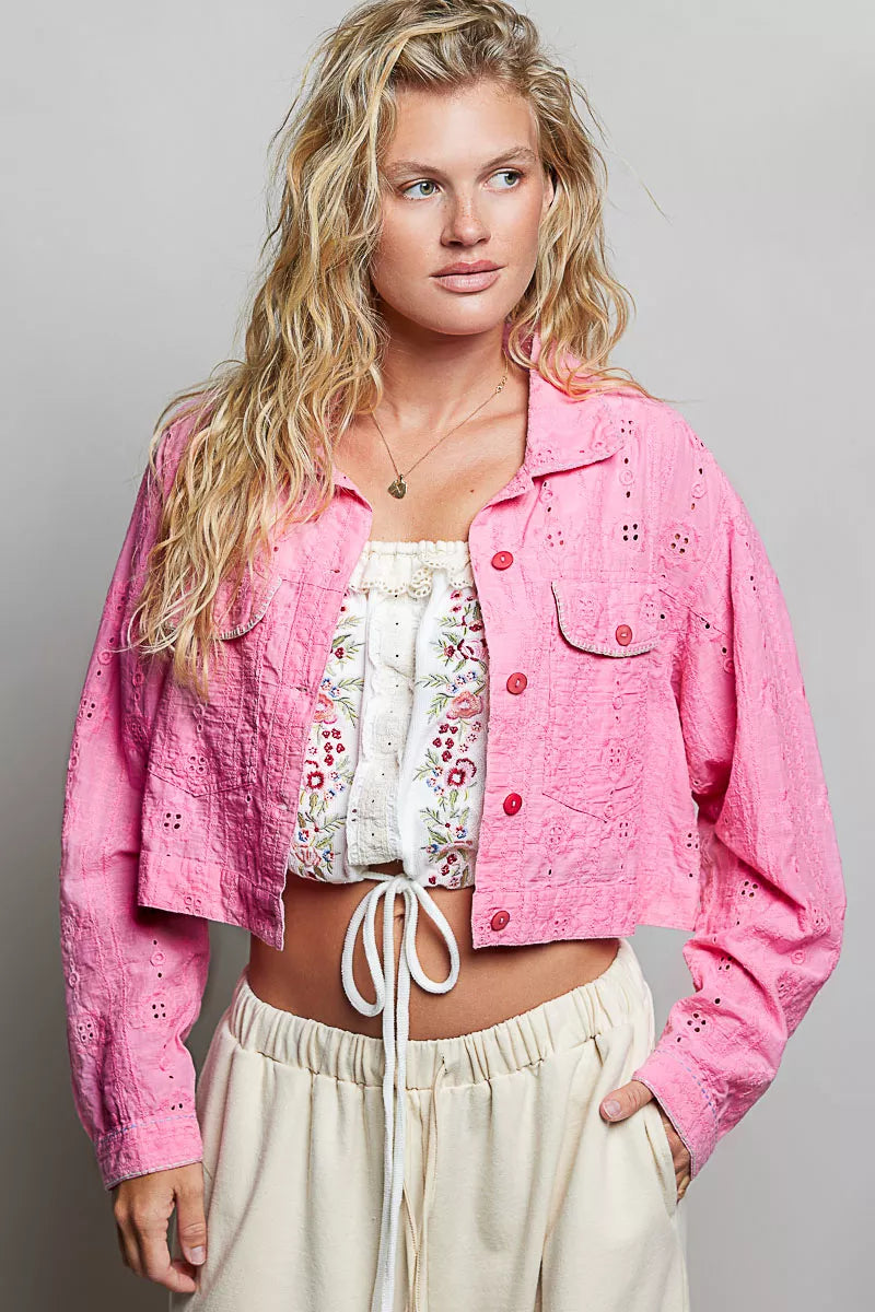 Woman wearing a pink jacket over a white floral top and beige pants on a gray background