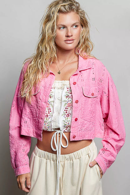 Woman wearing a pink jacket over a white floral top and beige pants on a gray background