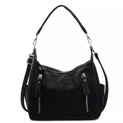 A black suede hobo shoulder bag with silver-tone hardware, featuring a top zipper, two front zipper pockets with leather pull tabs, and a detachable shoulder strap, shown against a plain white background.