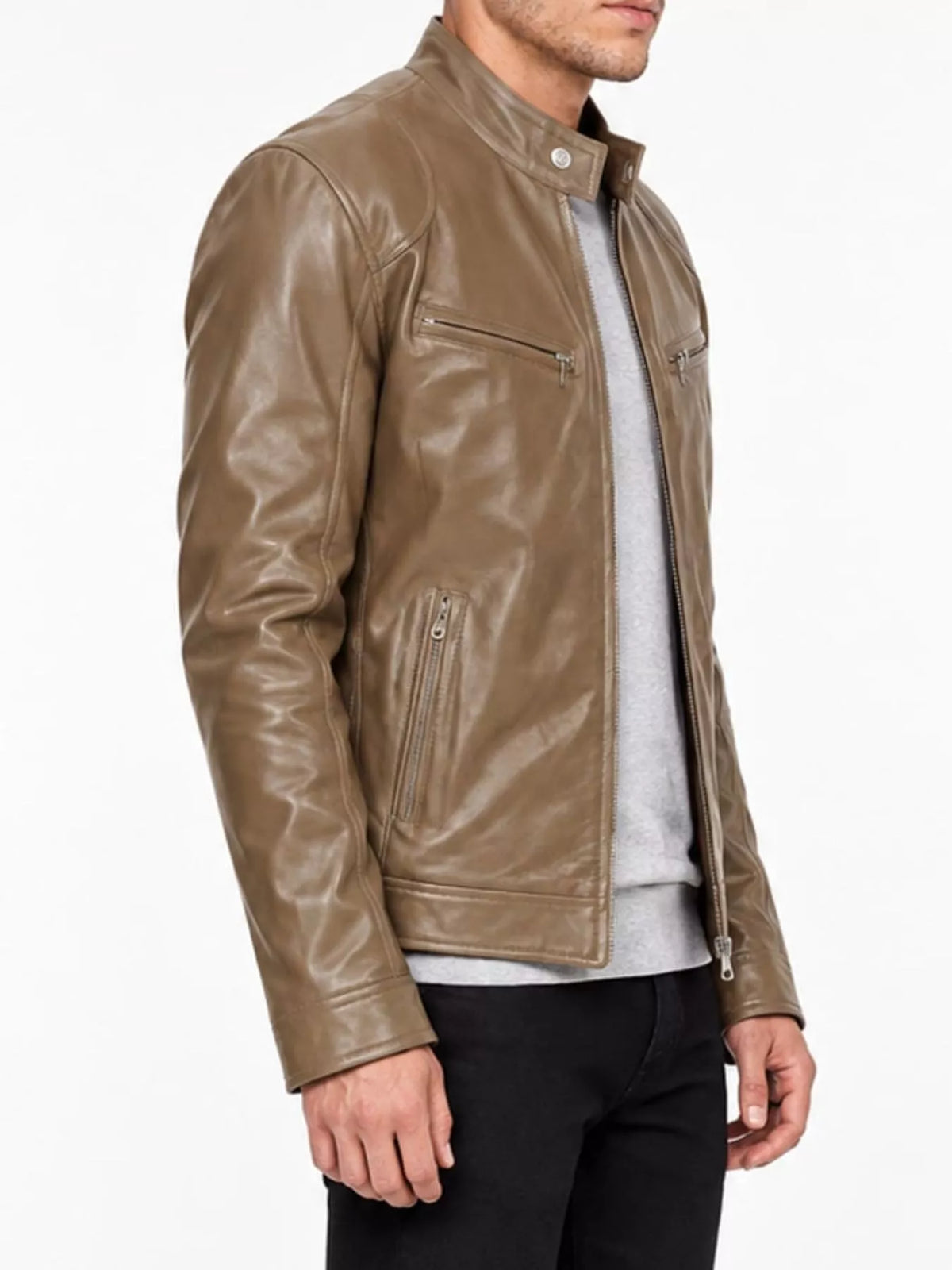 A man wearing a brown leather motorcycle jacket over a light gray sweater and black pants, shown from the chest down against a plain white background.