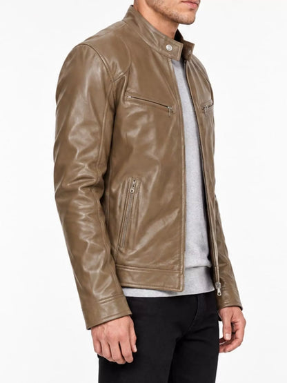 A man wearing a brown leather motorcycle jacket over a light gray sweater and black pants, shown from the chest down against a plain white background.