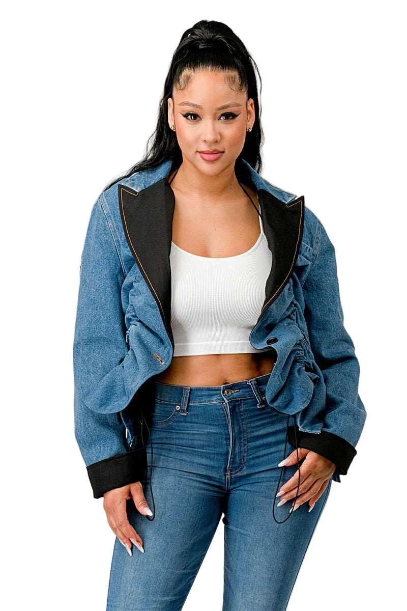 Woman wearing a denim jacket with black trim, white top, and blue jeans on a plain background