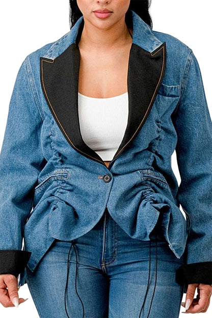A woman wearing a blue denim blazer-style jacket with black satin lapels and gathered ruffle details at the waist, paired with blue jeans and a white top.