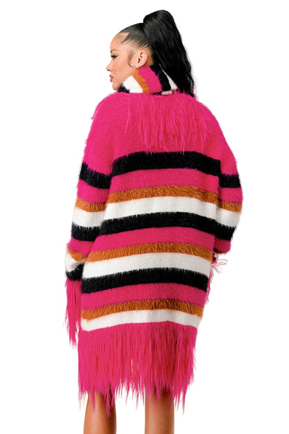 Woman wearing a colorful striped cardigan with fringe on a plain background