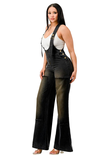 Woman wearing black overalls with a white top on a plain background