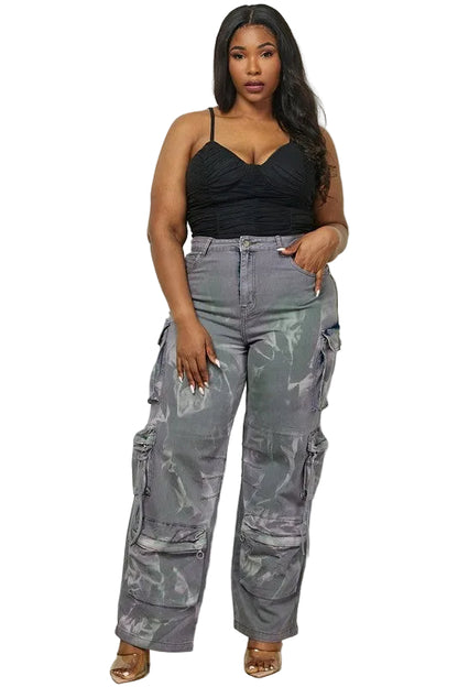Woman wearing a black top and gray camouflage pants against a white paneled wall.