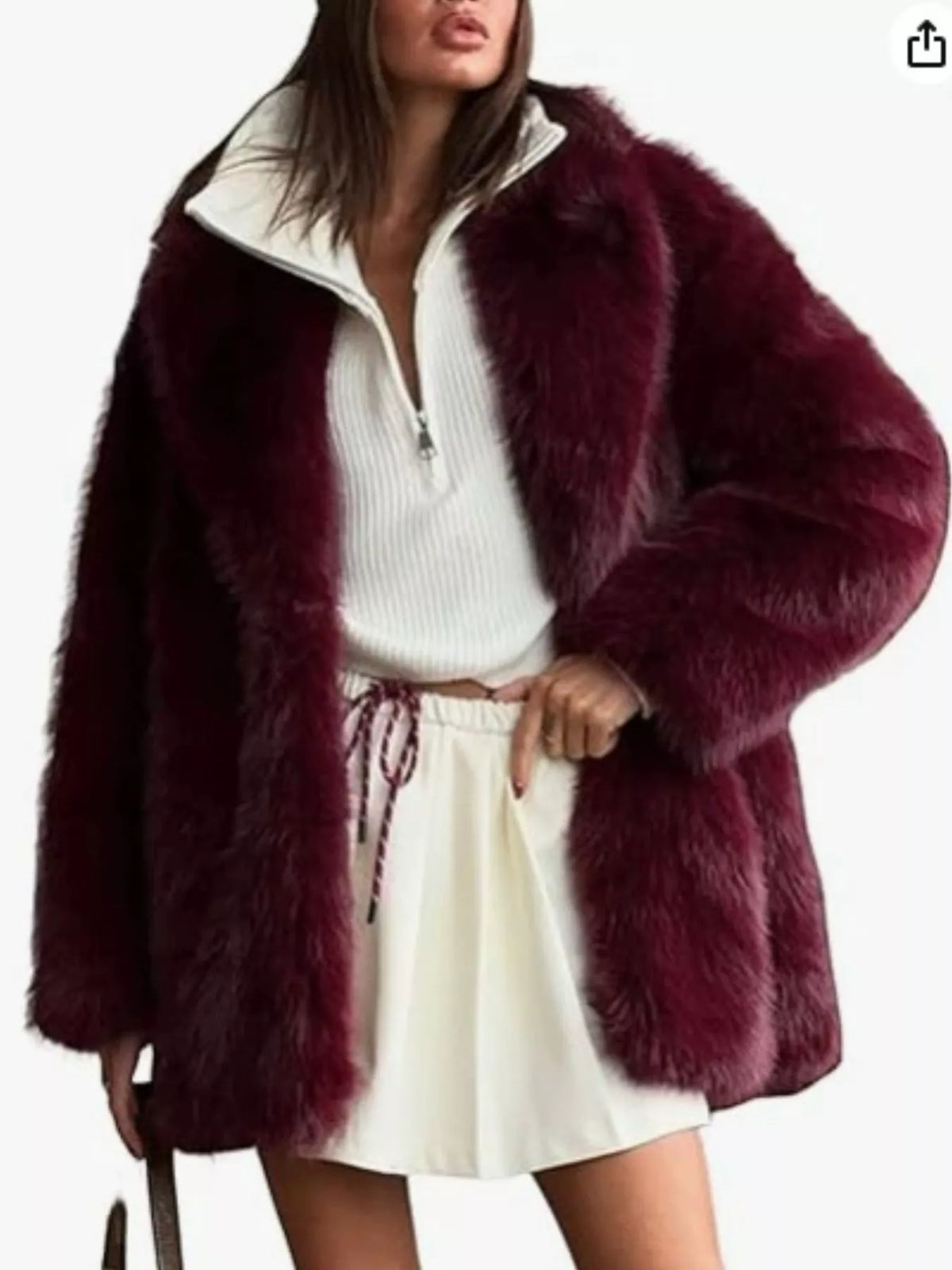 A woman wearing a plush, deep burgundy faux fur jacket over a white ribbed half-zip top and a white pleated mini skirt, shown against a plain white background.