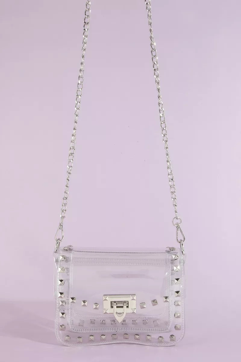 Clear handbag with silver studs and chain strap on a light purple background