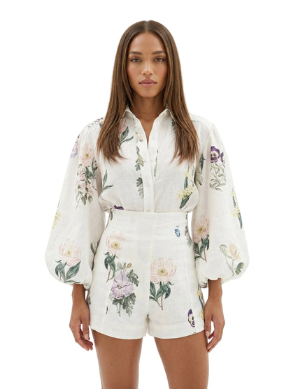 A woman modeling a matching white two-piece set with a delicate floral print, featuring a long-sleeve button-up shirt and coordinating shorts, set against a plain white studio background.