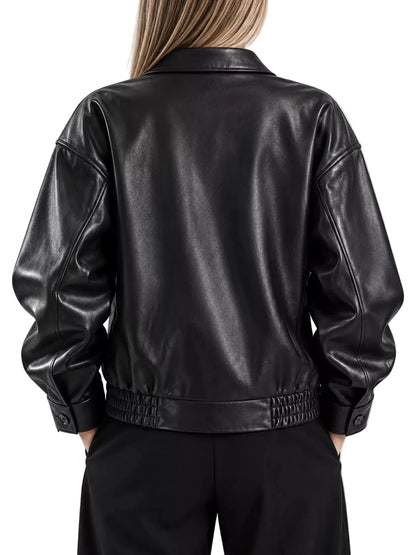 A person shown from the back wearing a black faux-leather jacket with a smooth finish, gathered elastic waistband, and buttoned cuffs, paired with black pants against a light gray studio background.