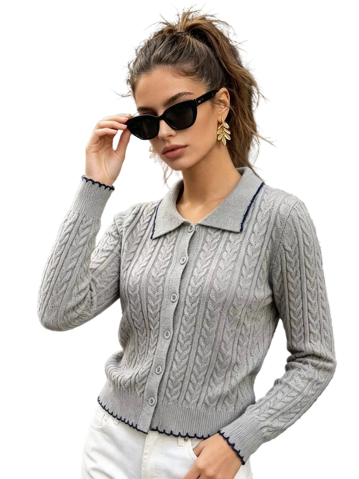 A woman wearing a light gray cable-knit button-up cardigan with dark navy trim, styled with white pants, black sunglasses, and gold earrings, standing in front of a storefront.