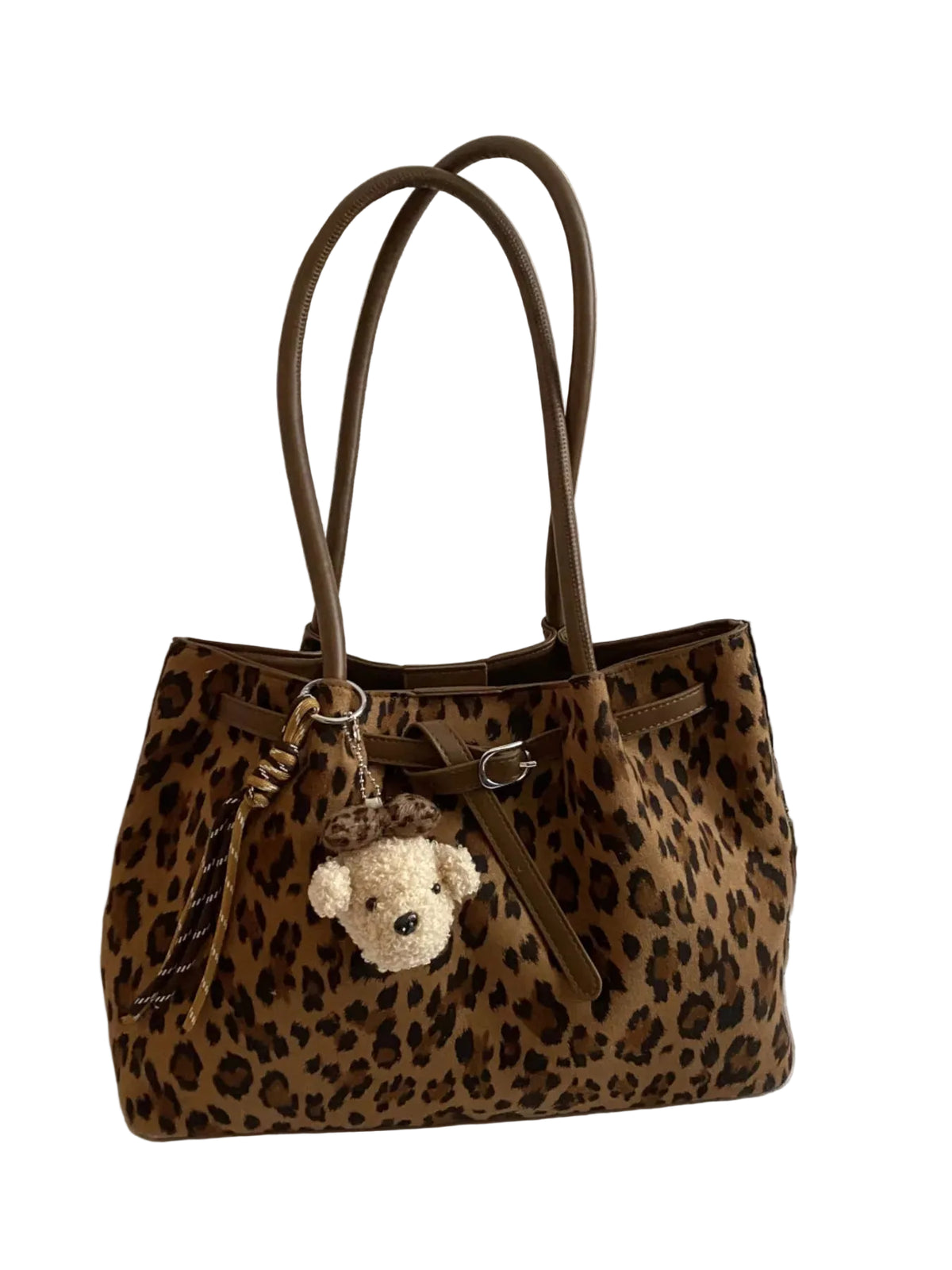A leopard print tote bag with brown handles and a small plush teddy bear keychain, displayed on a white fabric surface next to a laptop and headphones.