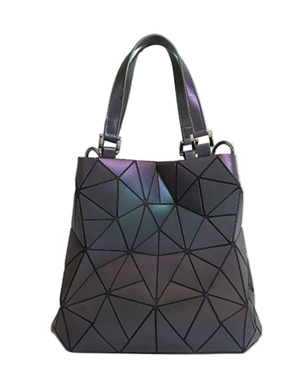 A geometric faceted handbag with an iridescent dark purple and blue finish, featuring dual top handles and silver-tone hardware, set against a plain beige background.