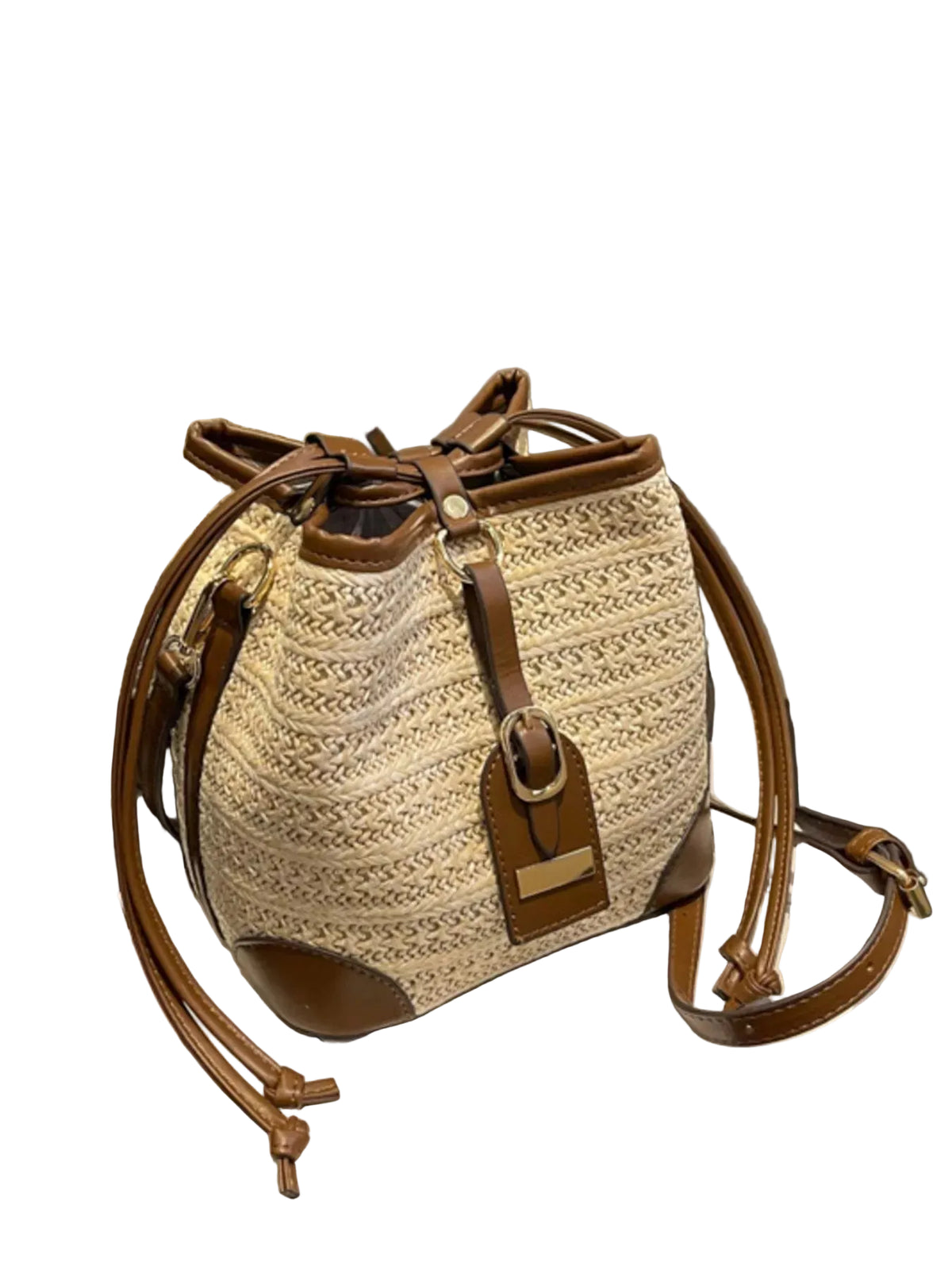 A woven straw bucket bag with brown leather trim and straps, displayed on a white book in an indoor setting.