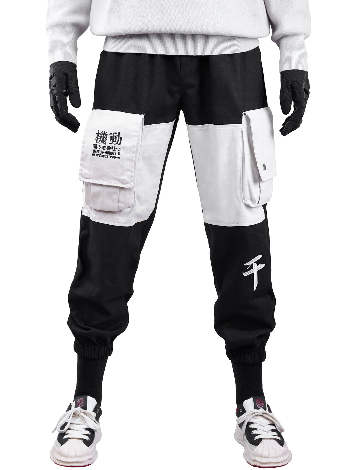 A person wearing black and white color-block cargo jogger pants with black gloves and white sneakers, shown from the chest down against a plain white background.